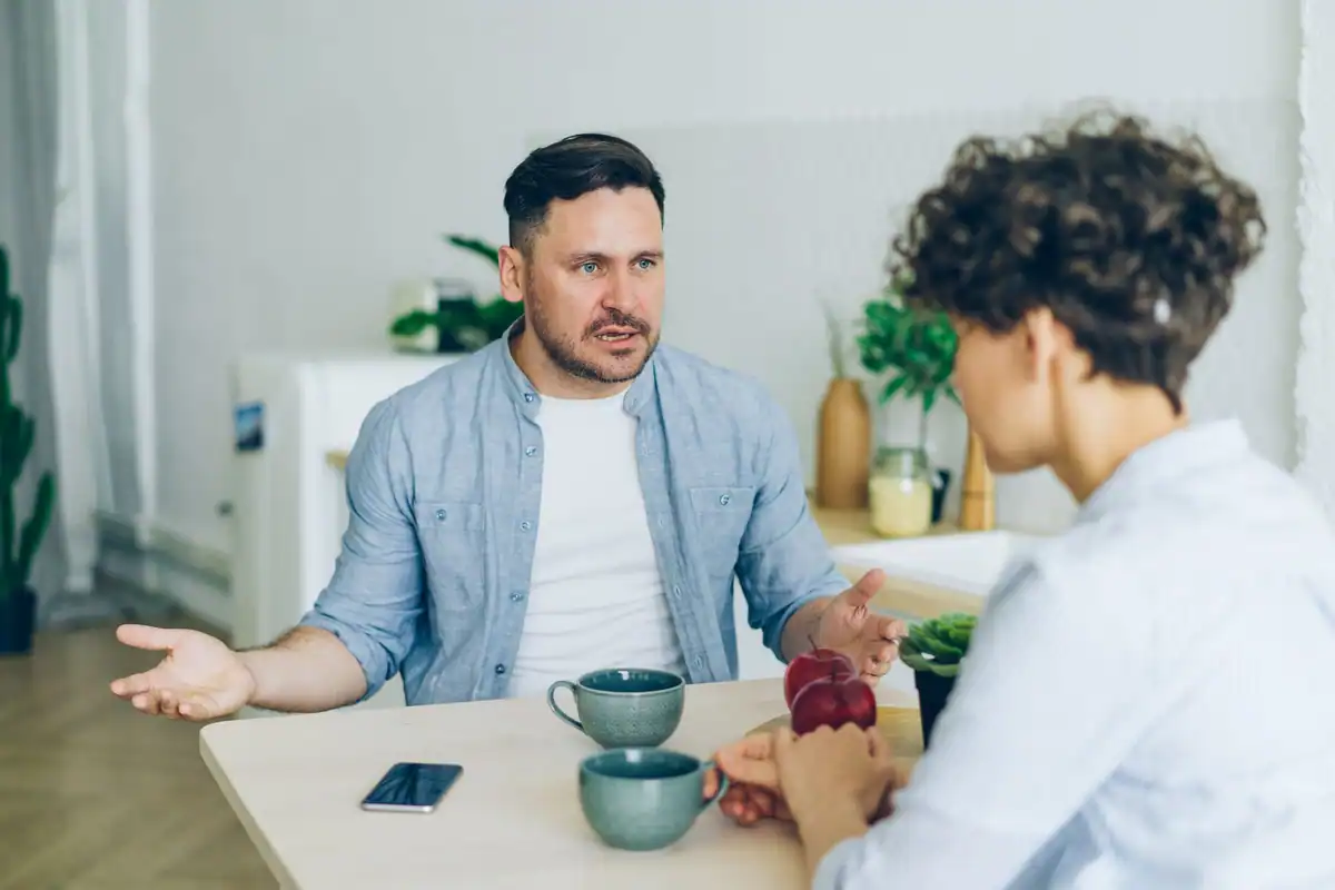 Doi adulți care discută la masa din bucătărie, cu cești de cafea în față