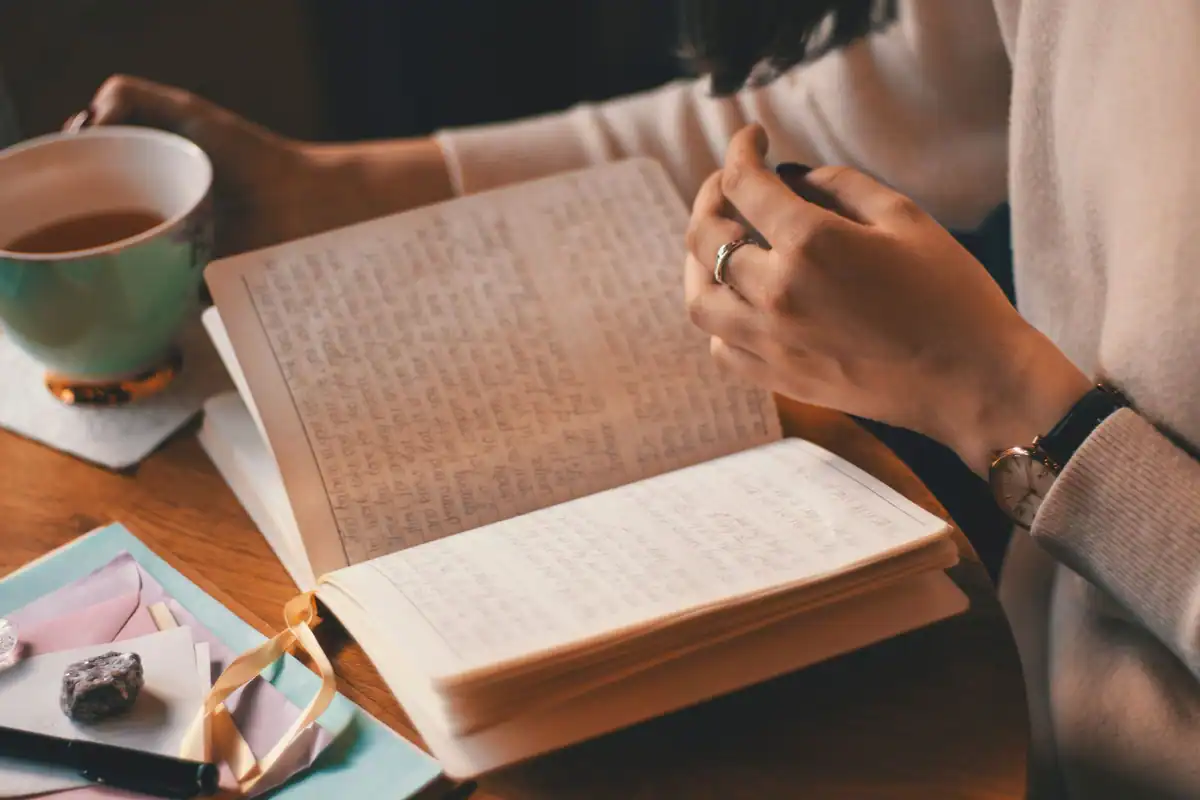 Femeie care își notează gândurile într-un jurnal, cu o cană de cafea alături