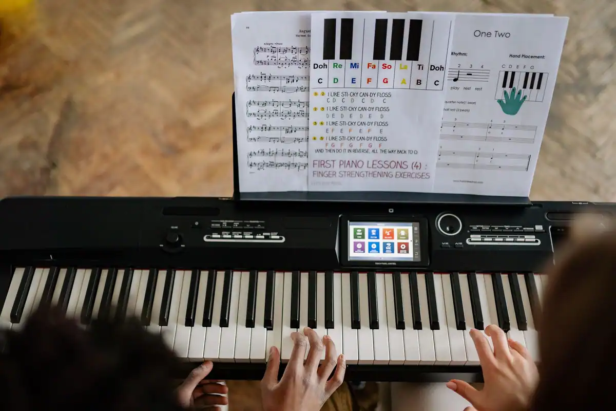 Adulți care învață să cânte la pian după partituri, văzuți de sus