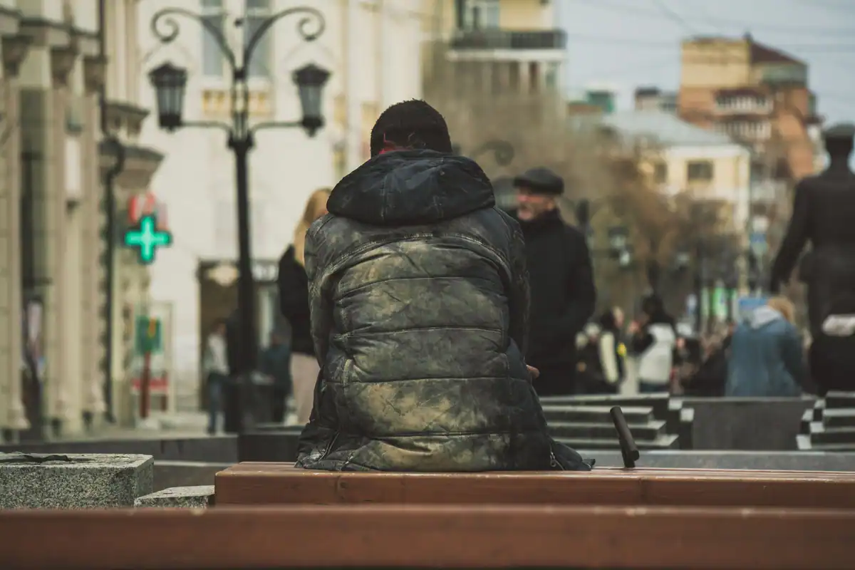 Bărbat singur pe o bancă, pe o stradă aglomerată, privind trecătorii