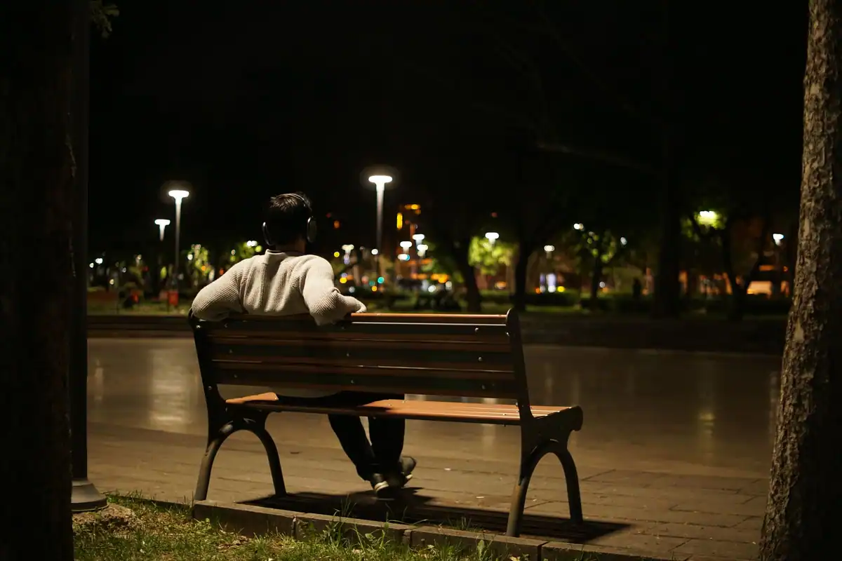Bărbat cu căști singur pe o bancă în parc, noaptea, sub felinare
