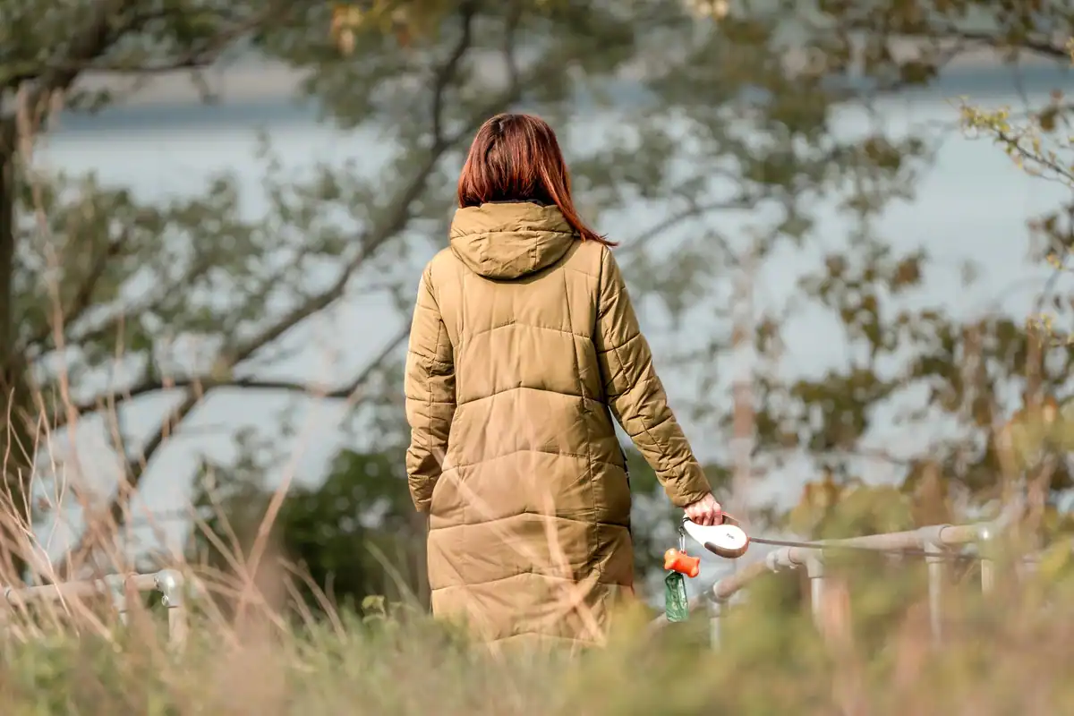 Femeie care se plimbă printr-un parc de toamnă, pe lângă un lac